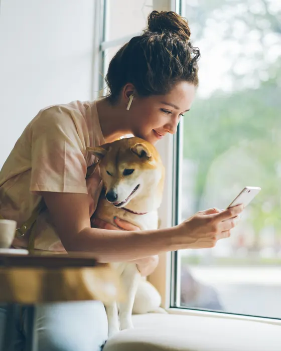 Cuidadora abrazando a un shiba junto a la ventana mientras le toma una foto para su dueño